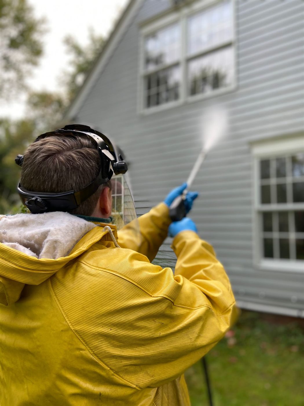 Technician in protective gear power washing the siding of a house